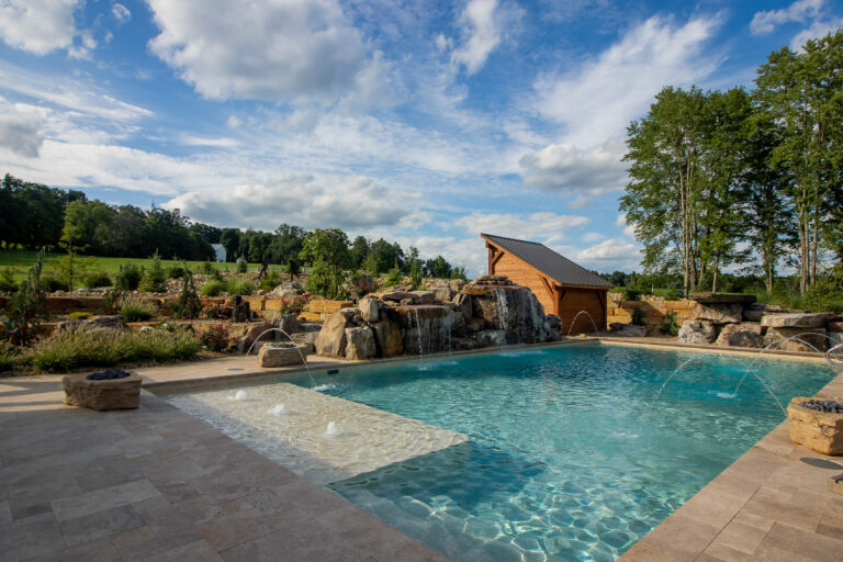 Custom backyard pool with a rock waterfall and covered pavilion at dusk