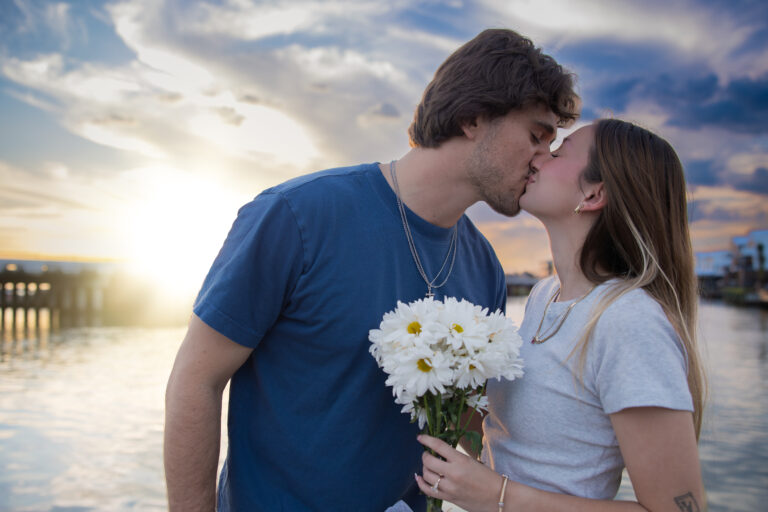 Engagement portrait of a couple holding daisies at sunset on a pier